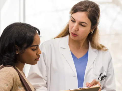 A young woman looks at a clipboard with her female doctor.