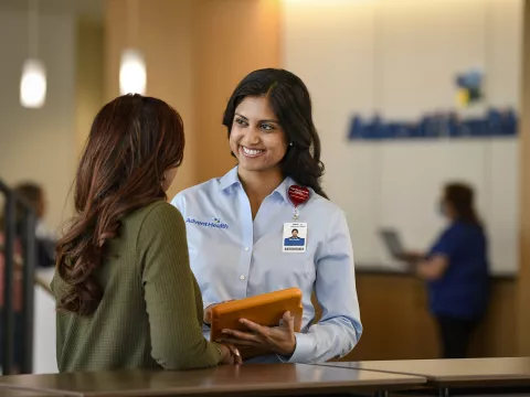 A smiling AdventHealth Employee welcomes a patient at the front desk.