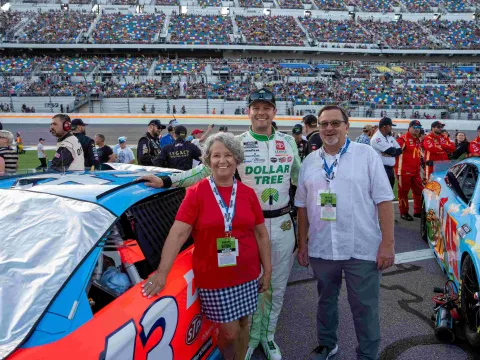 During the Coke Zero Sugar 400, cancer survivor Corrine Graczewski smiles alongside her husband Steve and the car driven by NASCAR Cup Series driver Erik Jones. 