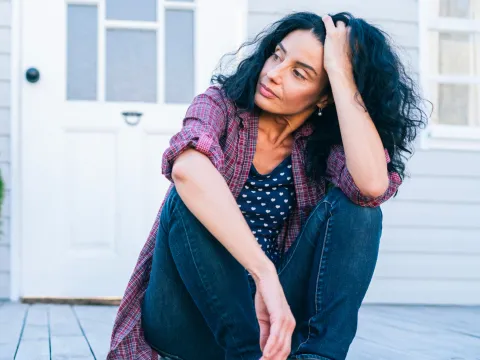 A woman sitting on the porch looking concerned.