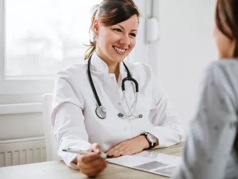 A friendly doctor meets a patient for the first time. They are both sitting at a desk, facing each other.