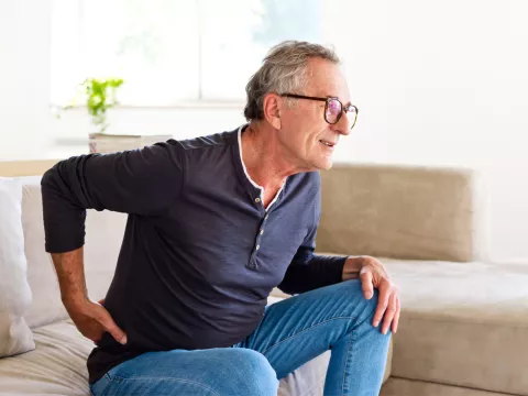Older man holding his back with his hand while getting up off the couch.