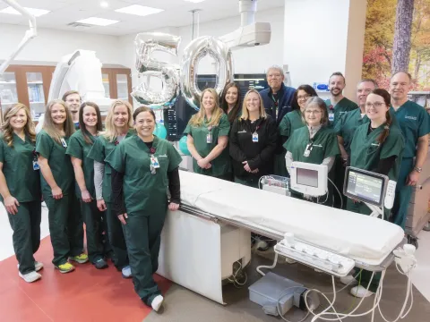 AdventHealth Redmond's Cath Lab team stands in their suite. There are two large, silver balloons in the background that read "50". 