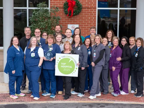 A group of AdventHealth Murray team members in different colored scrubs stand together. The woman in the front, center position is holding a sign that reads "The Leapfrog Group, 2025 Top Hospital"