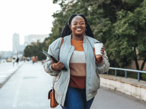 A Woman Walks Down a City Sidewalk with a Cup of Coffee
