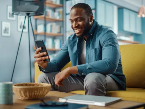 A smiling man looking at his phone while sitting on a couch
