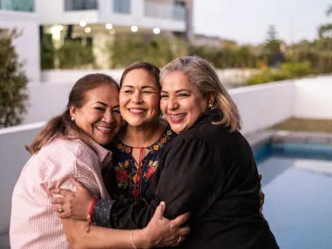 Female Latin friends hugging each other and laughing at home
