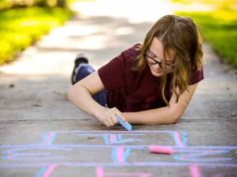 Girl chalks hopscotch game on sidewalk