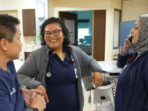 A group of nurses chat on a hospital unit floor. 