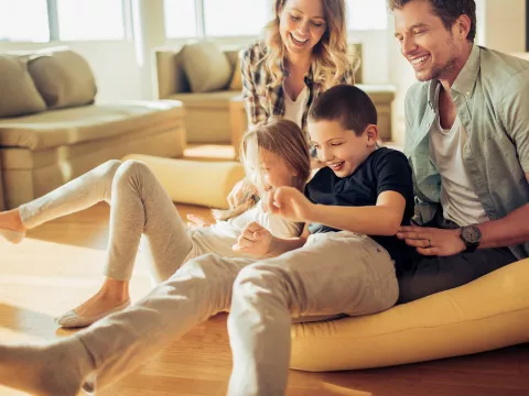 Family playing and laughing together in a sun filled living room of their house.