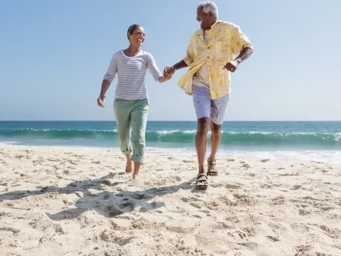 A couple holds hands while walking through sand on the beach.