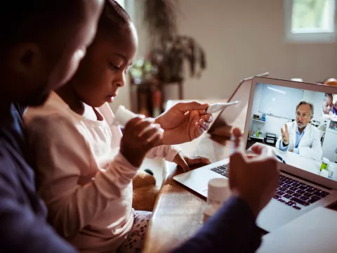 A father and daughter talking to a doctor on their laptop