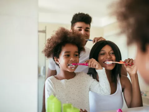 A young girl brushes her teeth with her parents as examples