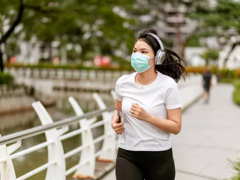 Woman running in a park outside while wearing a mask.