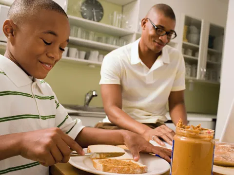 Father and son make peanut butter sandwiches together.