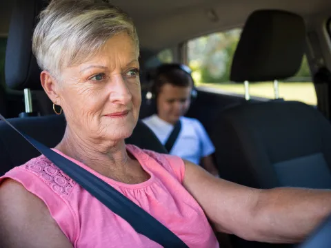 A grandmother driving with her grandson in the back seat.