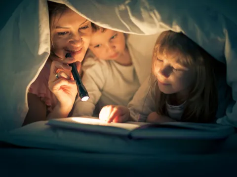 A mother, daughter, and son reading bedtime stories underneath the sheets
