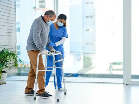 A nurse assisting a senior man while using a walker