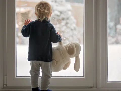A toddler looks at the snow through a window.