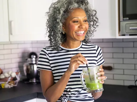 A woman drinking a healthy green smoothie in her kitchen.