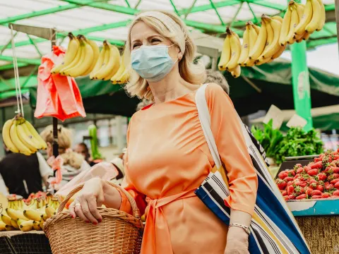 A woman wearing a mask at an outdoor farmers market.