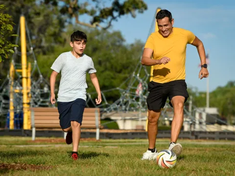 Son and father playing soccer in park