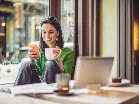 Hispanic woman with tea holding her phone and smiling.