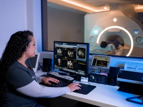 Imaging technician reviewing scans on a computer while a patient is receiving a MRI scan.