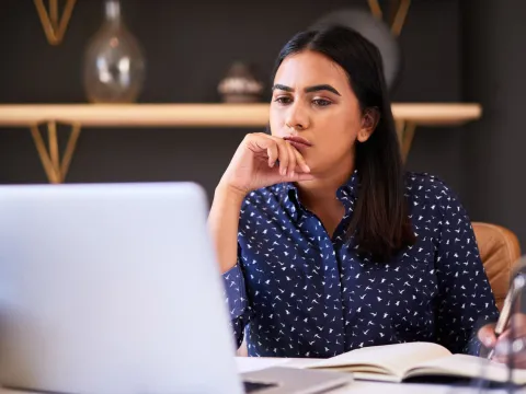 A woman looking thoughtfully at her laptop