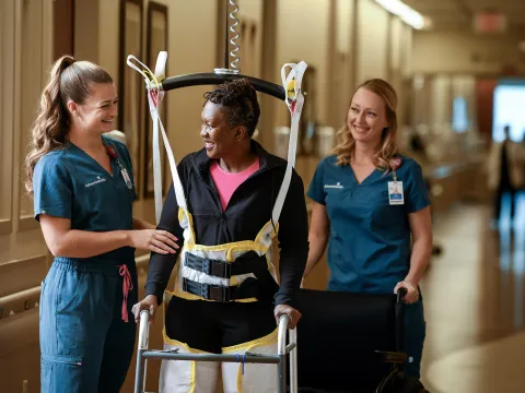 A woman walking with the help of two healthcare workers.