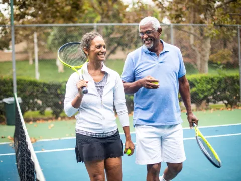 Two adults, walking off of the tennis court, talking to each other and having a great time.