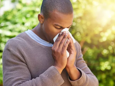 A black man blowing his nose while outside.
