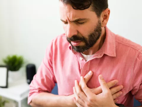 A main sitting and placing hands over chest in pain.