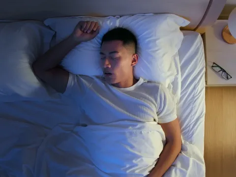 Man sleeping on his back in a bed.