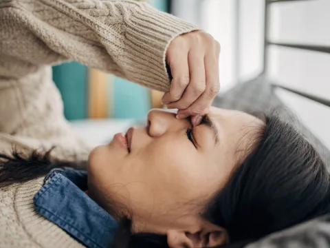 A woman with a headache holds her fingers to the bridge of her nose.
