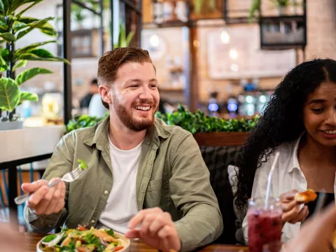 A young man eating health food a table with friends.