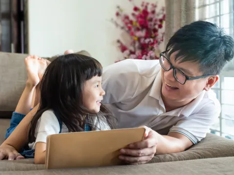 A father and his daughter lying on the floor reading together.