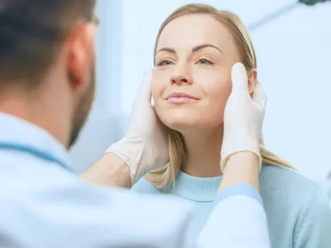 A doctor holds his hands to each side of a woman's face.