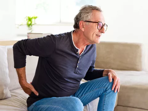 A senior gentleman showing discomfort while getting up from his couch