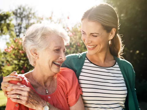 A senior woman with her adult daughter walking together outdoors.