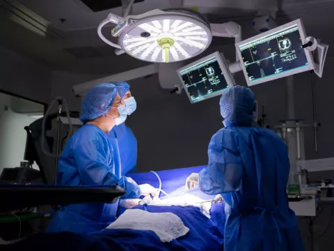A surgical staff of three people performing a surgery in an operating room.