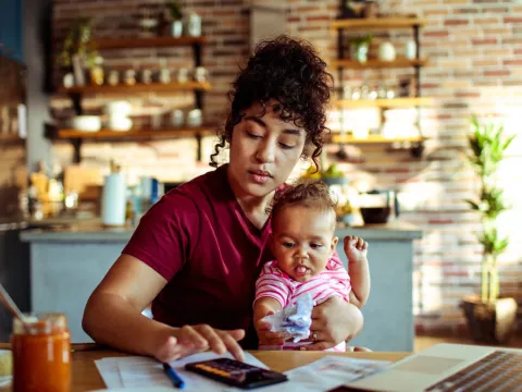 A mother holding her baby while using a calculator