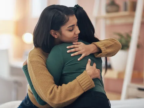 Two women hugging while at home.