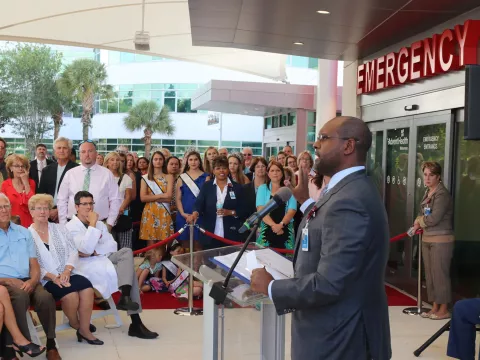 A crowd of people listening to the grand opening speech from an AdventHealth employee