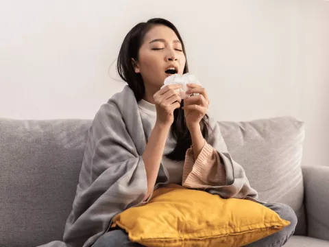 A woman sneezing into a tissue.