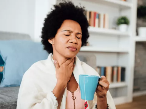 A sick woman holds her hand to her neck.