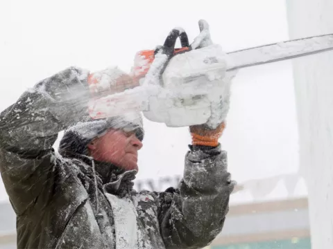 A man using a chainsaw to cut ice.