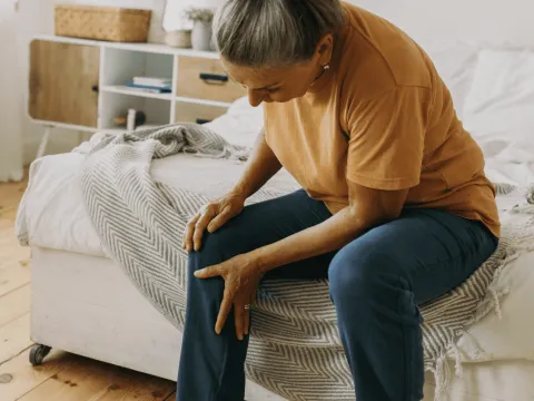 Woman sitting down at home and holding leg in pain.