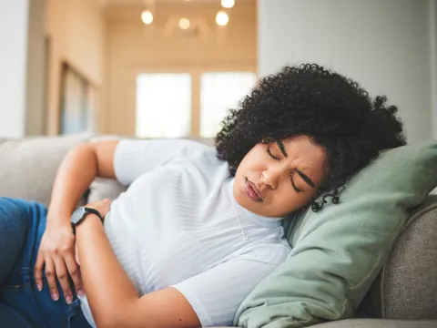 Woman laying on a couch at home holding her abdomen in pain.
