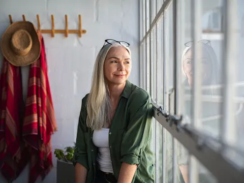 A mature woman sits at home and looks out a window